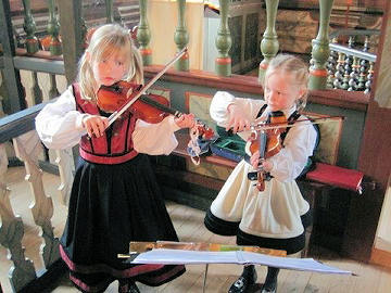 Bodil-Elise Fowels-Holberg (8) en haar sussie, Maria Fowels-Holberg (6) speel viool tydens die doop van hulle boetie, Bror Benjamin Fowels-Holberg. Hulle pa, wat predikant van die Flosta gemeente van die Noorweegse Kerk is, het die doop waargeneem