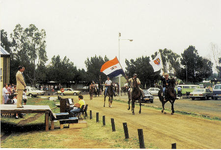 Die perdekommando kom by die Feesterrein aan, met burgemeester Gawie Swart wat op die podium die optog inwag. Kyk hoe wapper die landsvlag en die Henning vlag!